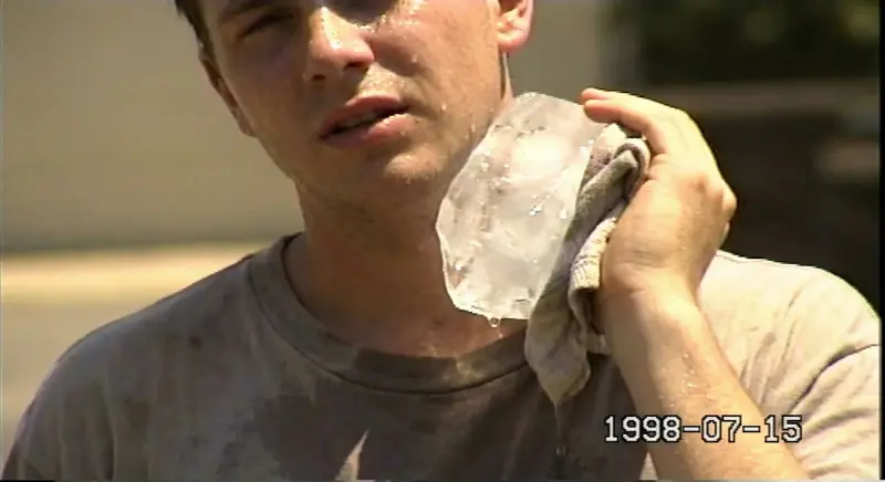 A lo-fi 90s digital portrait taken with a Sony Mavica floppy disk camera. A person holds a large, melting block of clear ice against their neck on a sweltering day. Grainy, pixelated, 640x480 aesthetic, slightly out of focus, harsh sun.